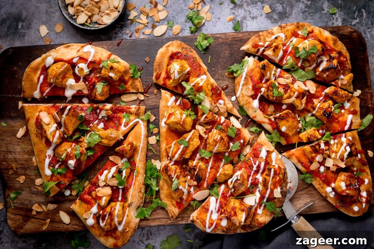 Chicken Tikka Pizza Recipe: Crispy Homemade Tandoori-Style Pizza 5 Overhead image of naan bread chicken tikka pizza topped with grilled chicken, coriander, sliced almonds, red sauce, and a white drizzle, sliced and served on a wooden board.