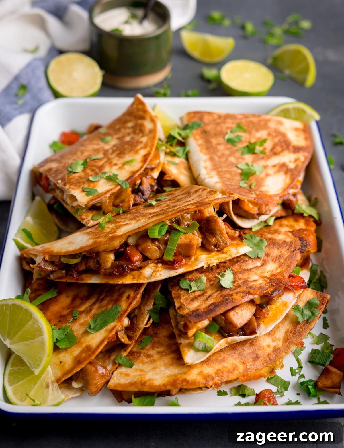 A tray of chicken quesadillas filled with vegetables and garnished with chopped coriander, served with lime wedges.