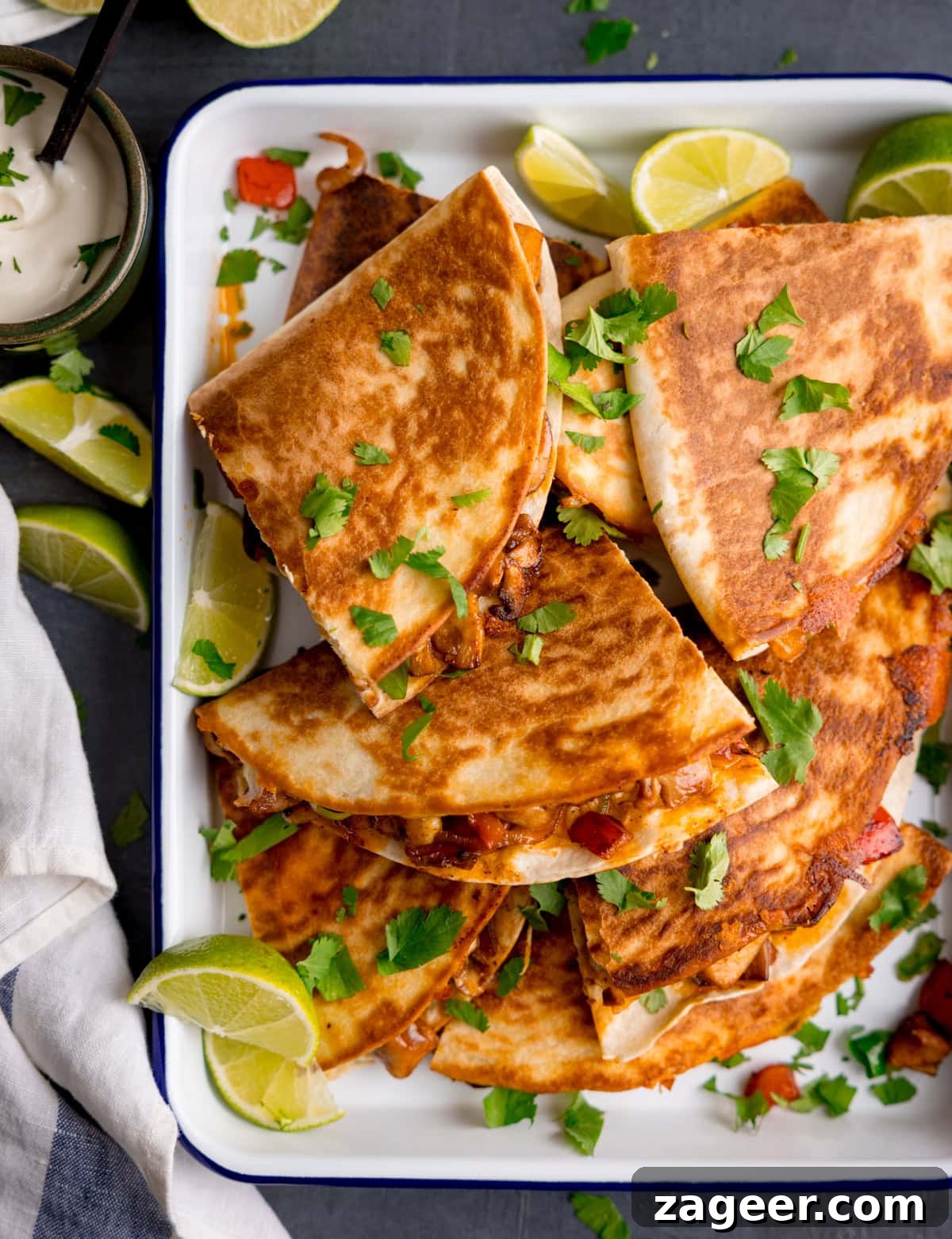 A platter of Chicken Quesadillas garnished with fresh coriander and lime wedges, served with a side of creamy dipping sauce.