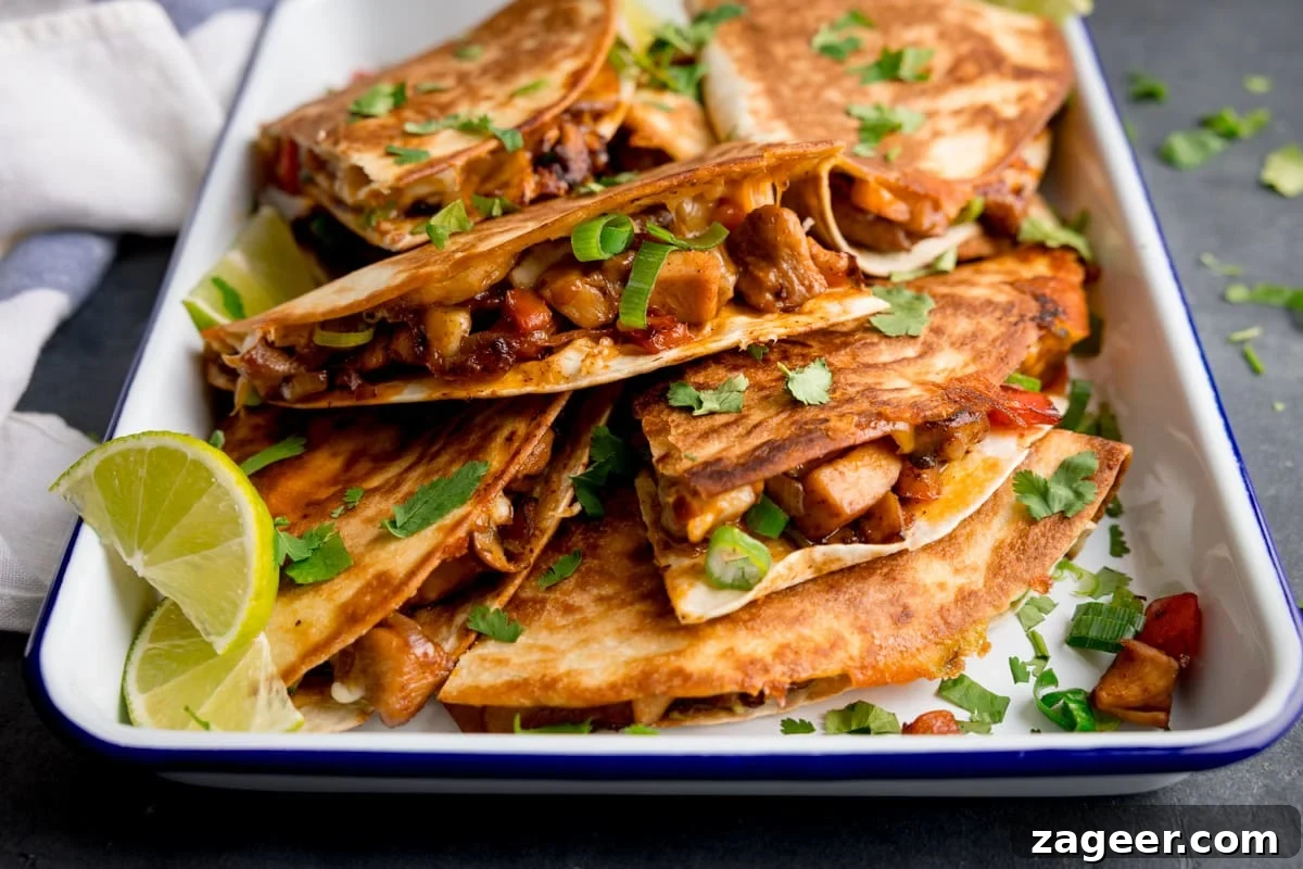 A tray of chicken quesadillas filled with vegetables and meat, garnished with chopped coriander and spring onions, with lime wedges on the side.