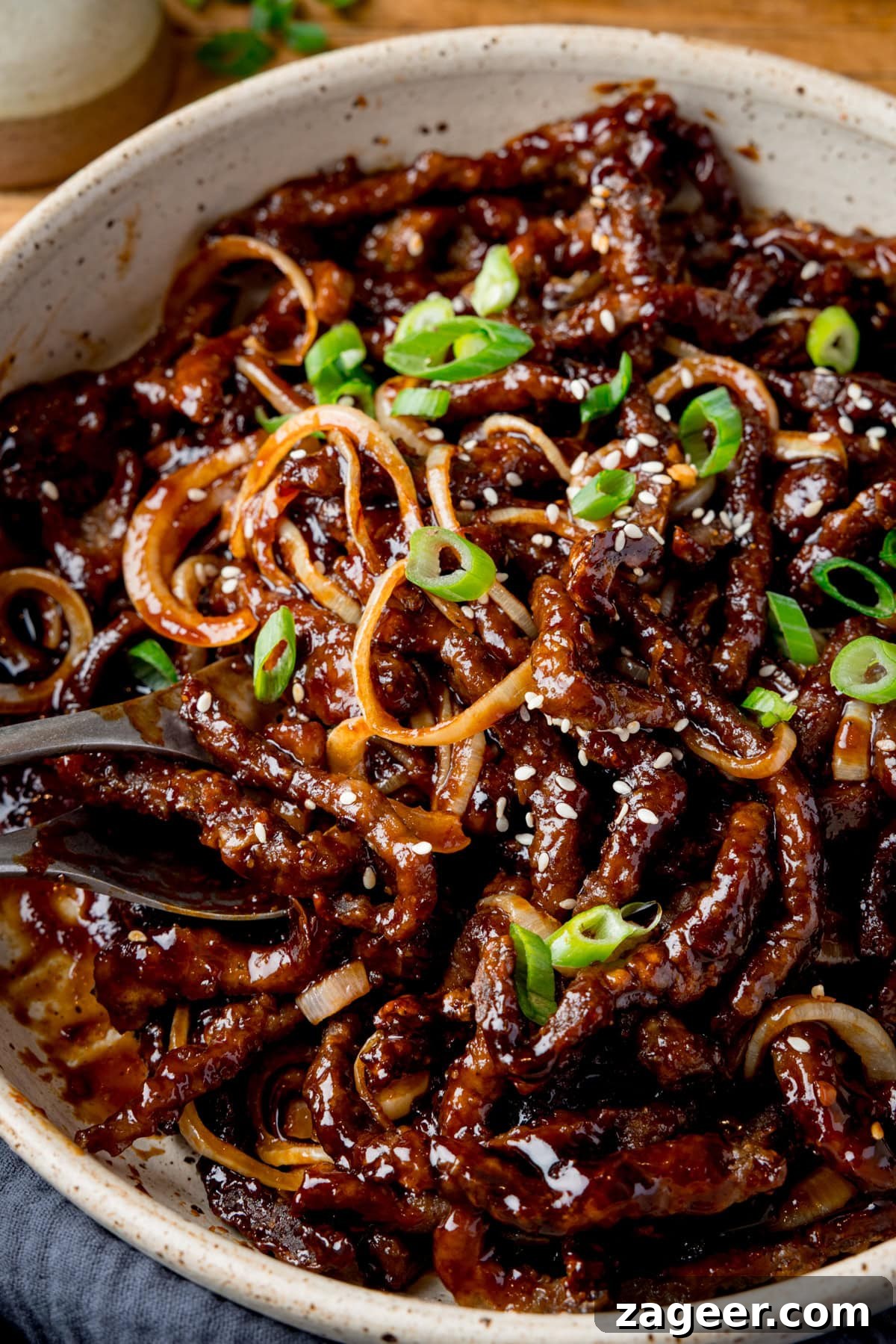 Crispy Chilli Beef in the Air Fryer: Quick Spicy Recipe 6 A close up of a light bowl filled with air fryer crispy chilli beef with onions, sesame seeds, and sliced spring onions.