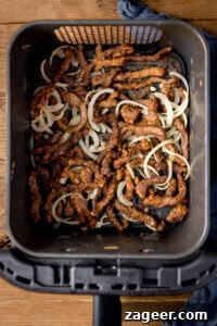 Crispy Chilli Beef in the Air Fryer: Quick Spicy Recipe 8 Strips of crispy beef and cooked onion slices in an air fryer basket, viewed from above.