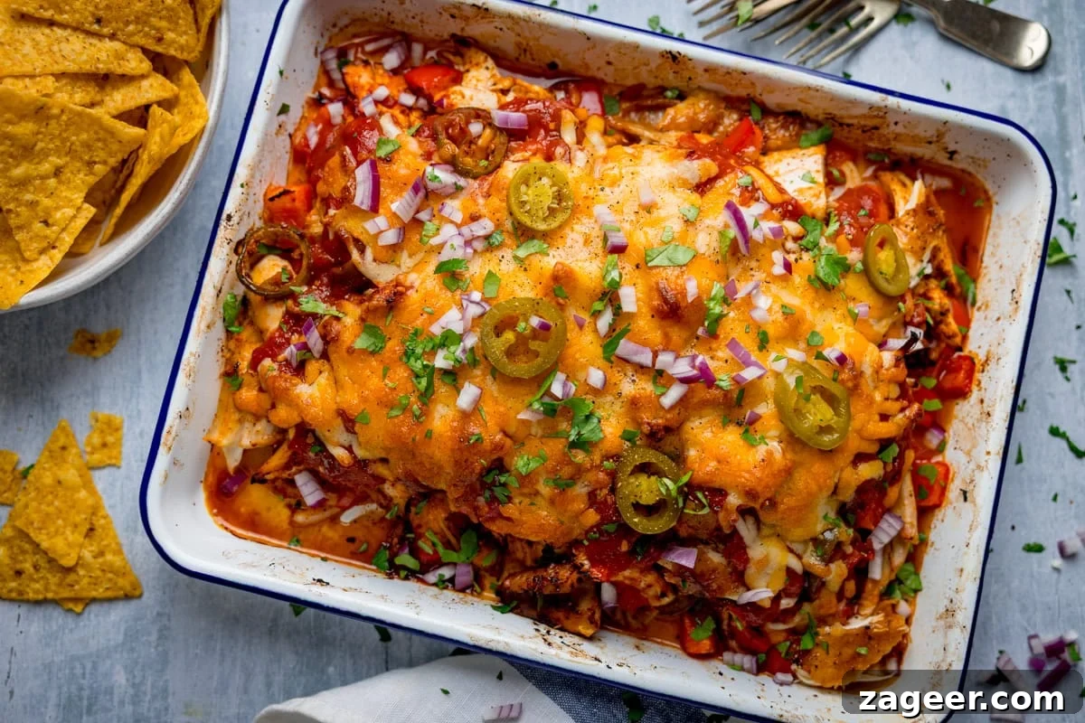 Slow-Cooker Salsa Chicken Recipe for Flavor-Packed Weeknight Meals 6 A baked dish of cheesy chicken salsa bake topped with chopped red onion, jalapeños, and coriander, served in a white tray next to a bowl of tortilla crisps.