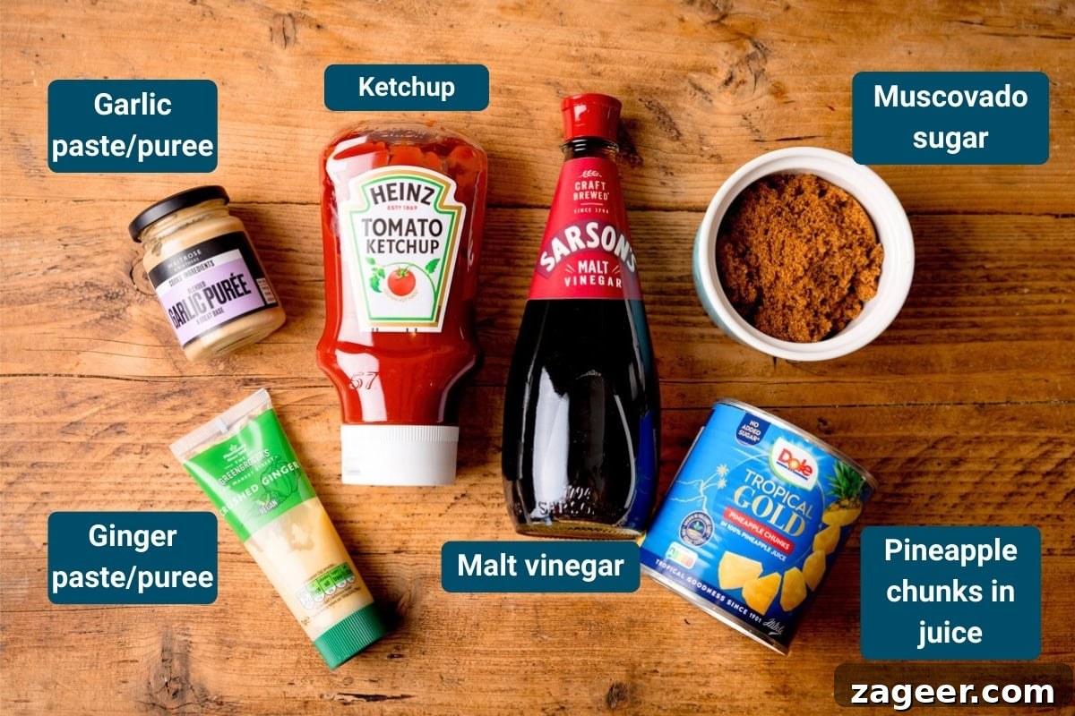 Crispy Air Fryer Sweet and Sour Chicken Recipe 5 Six ingredients on a wooden surface, including garlic paste, ginger paste, tomato ketchup, malt vinegar, muscovado sugar, and tinned pineapple in juice. Each item is labelled.