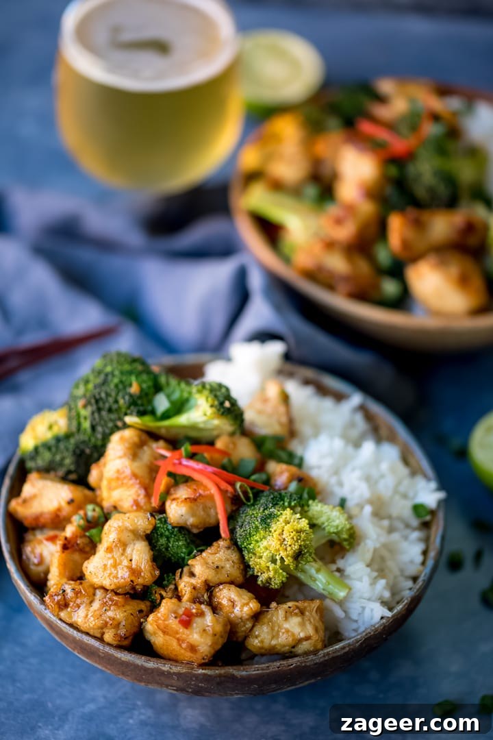Side on shot of crispy chicken with broccoli and rice in a bowl with blue background. Further bowl in background.