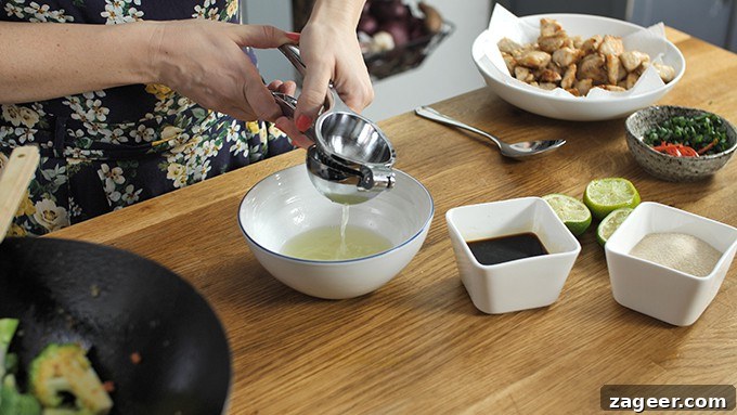 lime juice being squeezed into a bowl. Further ingredients on work surface.