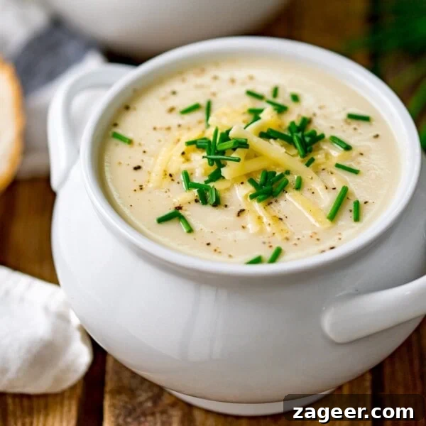 Cheddar and Vegetable Chowder Recipe with Creamy Veggies 12 Close up of a white bowl filled with cauliflower soup and topped with chopped chives, grated cheese and black pepper