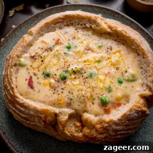 Cheddar and Vegetable Chowder Recipe with Creamy Veggies 13 A bread bowl filled with creamy vegetable chowder, topped with grated cheddar cheese and black pepper, served on a blue-green plate.