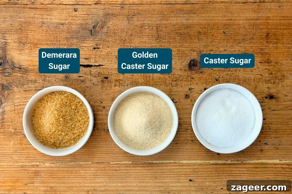 Classic Crème Brûlée Recipe: Silky Custard with Caramelized Sugar 5 Three small bowls on a wooden surface, each holding Demerara Sugar, Golden Caster Sugar, and Caster Sugar, labelled accordingly.