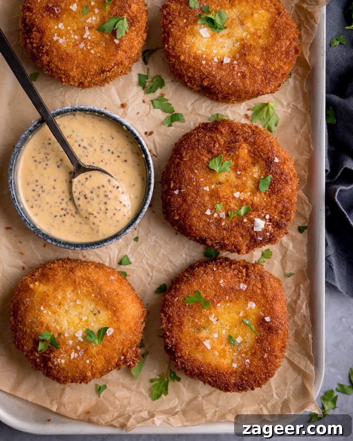 Crispy Tuna Fish Cakes with Lemon-Dill Sauce 2 Five breaded and fried tuna fishcakes on parchment paper, garnished with parsley, served with a small bowl of wholegrain mustard dip and a spoon.