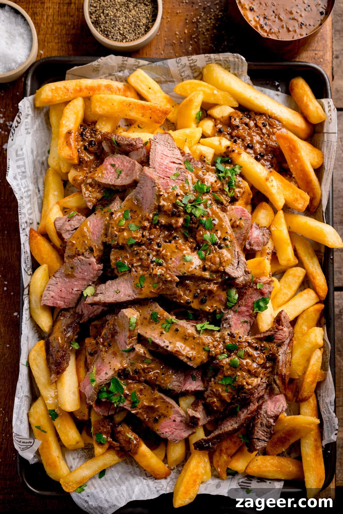 Steak Fries with Creamy Peppercorn Sauce 2 A tray of Steaky Chips—chips topped with sliced steak, peppercorn sauce, and chopped parsley, surrounded by little pots of salt, pepper, and extra peppercorn sauce.