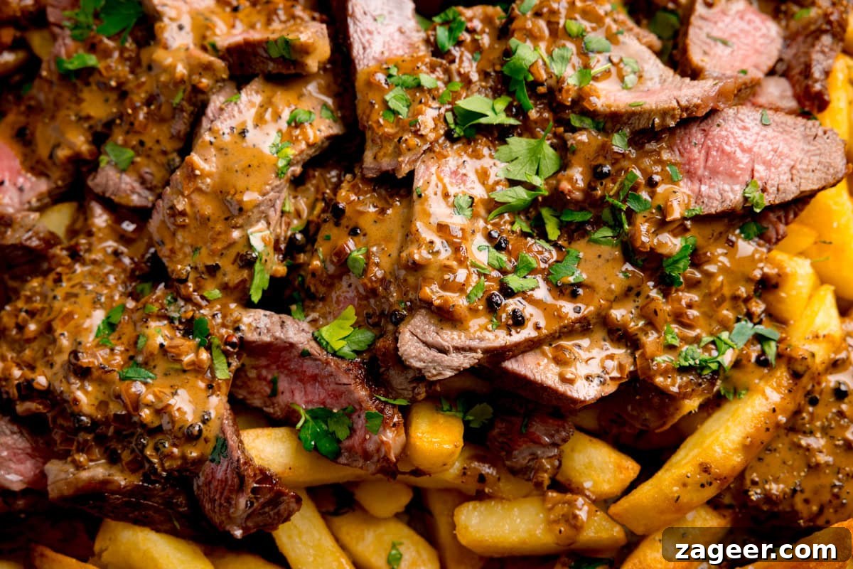 Steak Fries with Creamy Peppercorn Sauce 5 Close up wide image of sliced steak with Peppercorn Sauce and chopped parsley served over a bed of oven chips.