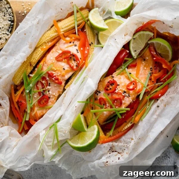 Tuscan Salmon with Creamy Lemon Orzo Recipe 11 Square image of two salmon fillets cooked in individual baking parchment parcels with slices of chilli, peppers, babycorn, carrot and spring onion. Also topped with wedges of lime.