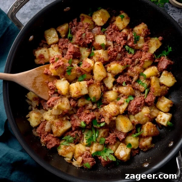 Crispy Potato and Bacon Hash Recipe for Breakfast or Brunch 10 Corned beef hash in a frying pan with a wooden spoon and parsley on top.