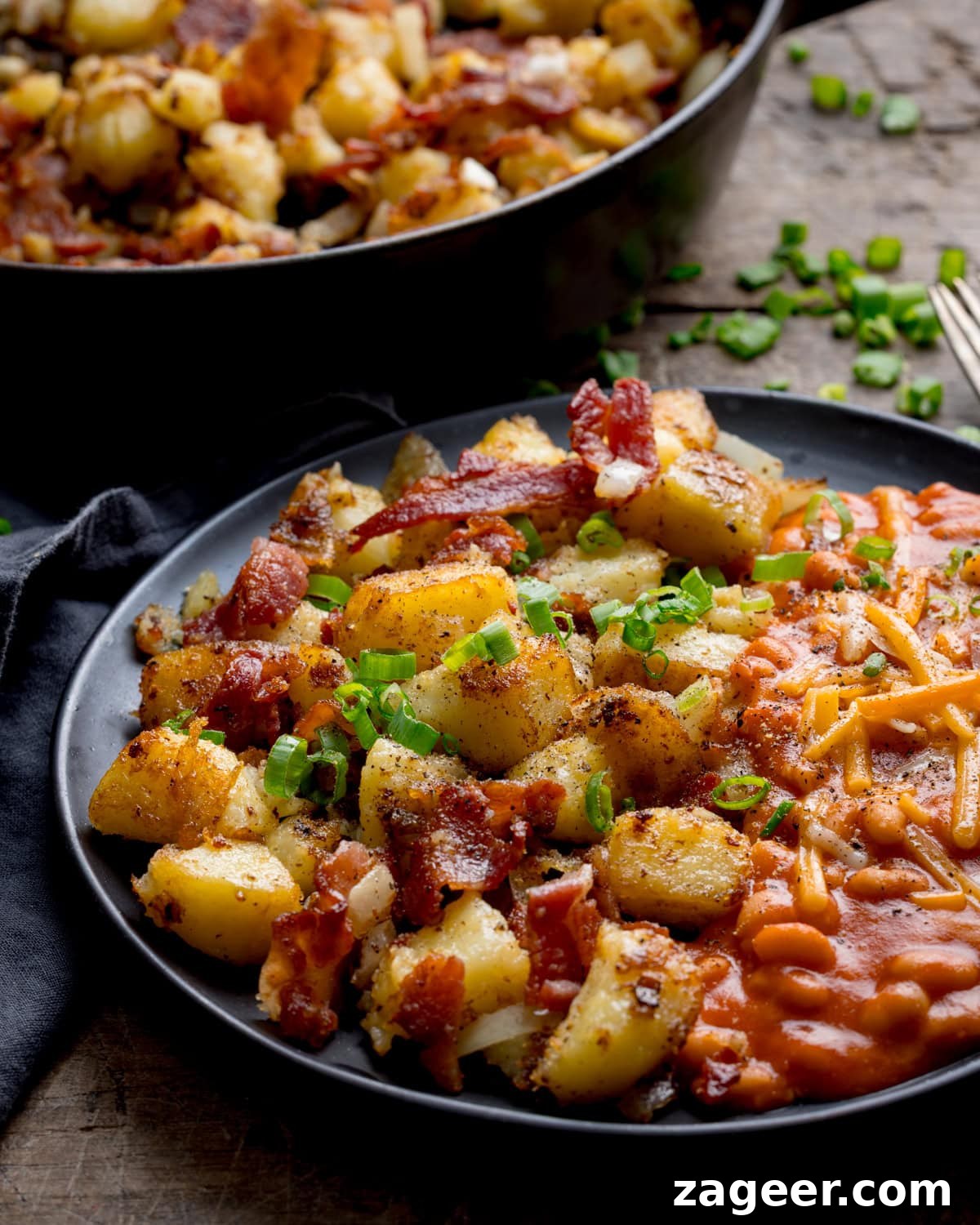 Crispy Potato and Bacon Hash Recipe for Breakfast or Brunch 5 A plate of seasoned potato and bacon hash with crispy bacon and chopped spring onions, served with baked beans topped with grated cheese.
