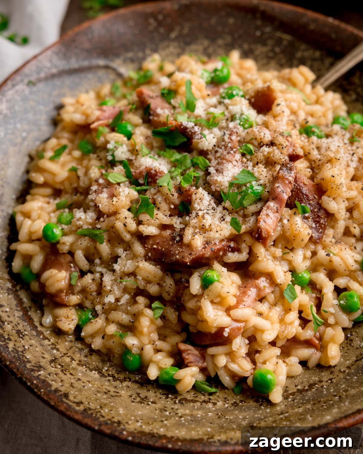 Creamy Ham and Spring Pea Risotto Recipe 2 Close up image of Ham and Pea Risotto served in a rustic brown bowl. There is a fork sticking out.