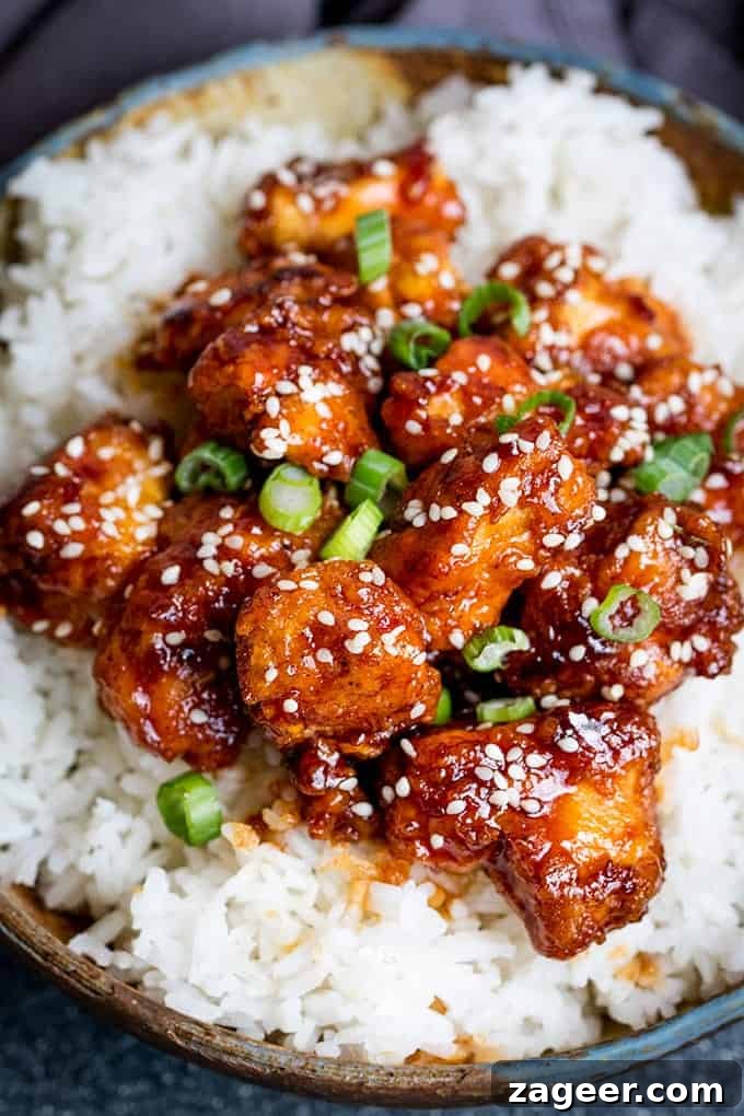 Crispy Sesame Chicken with Sticky Sweet-Savory Asian Sauce 2 Close up photo of Crispy Sesame Chicken with a Sticky Asian Sauce on a bed of rice in a stone bowl with a dark background