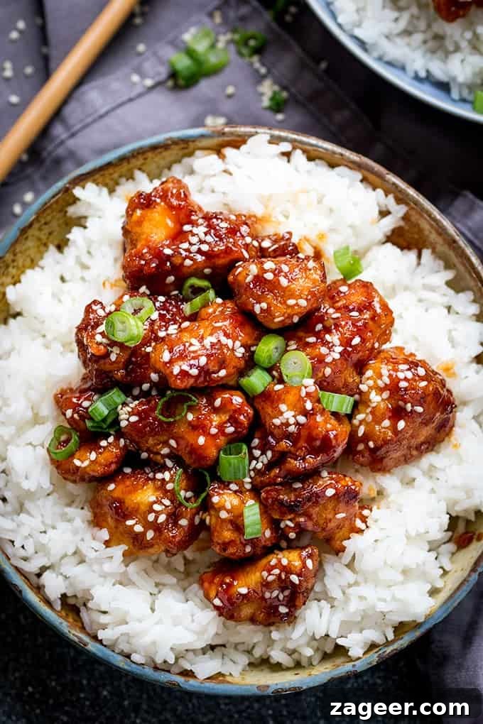 Crispy Sesame Chicken with Sticky Sweet-Savory Asian Sauce 4 Overhead picture of Crispy Sesame Chicken with a Sticky Asian Sauce on a bed of rice in a stone bowl with a dark background with chopsticks in the top left corner