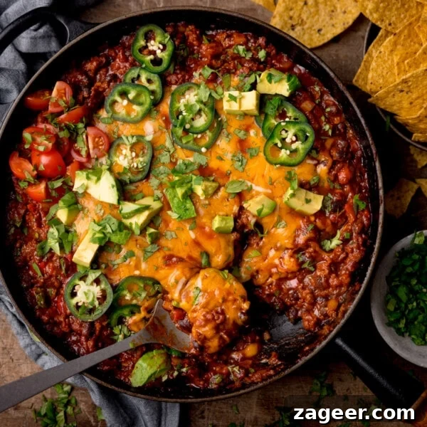 Tex-Mex minced beef in a black cast iron pan with cheese, jalapenos, coriander and avocados on top.