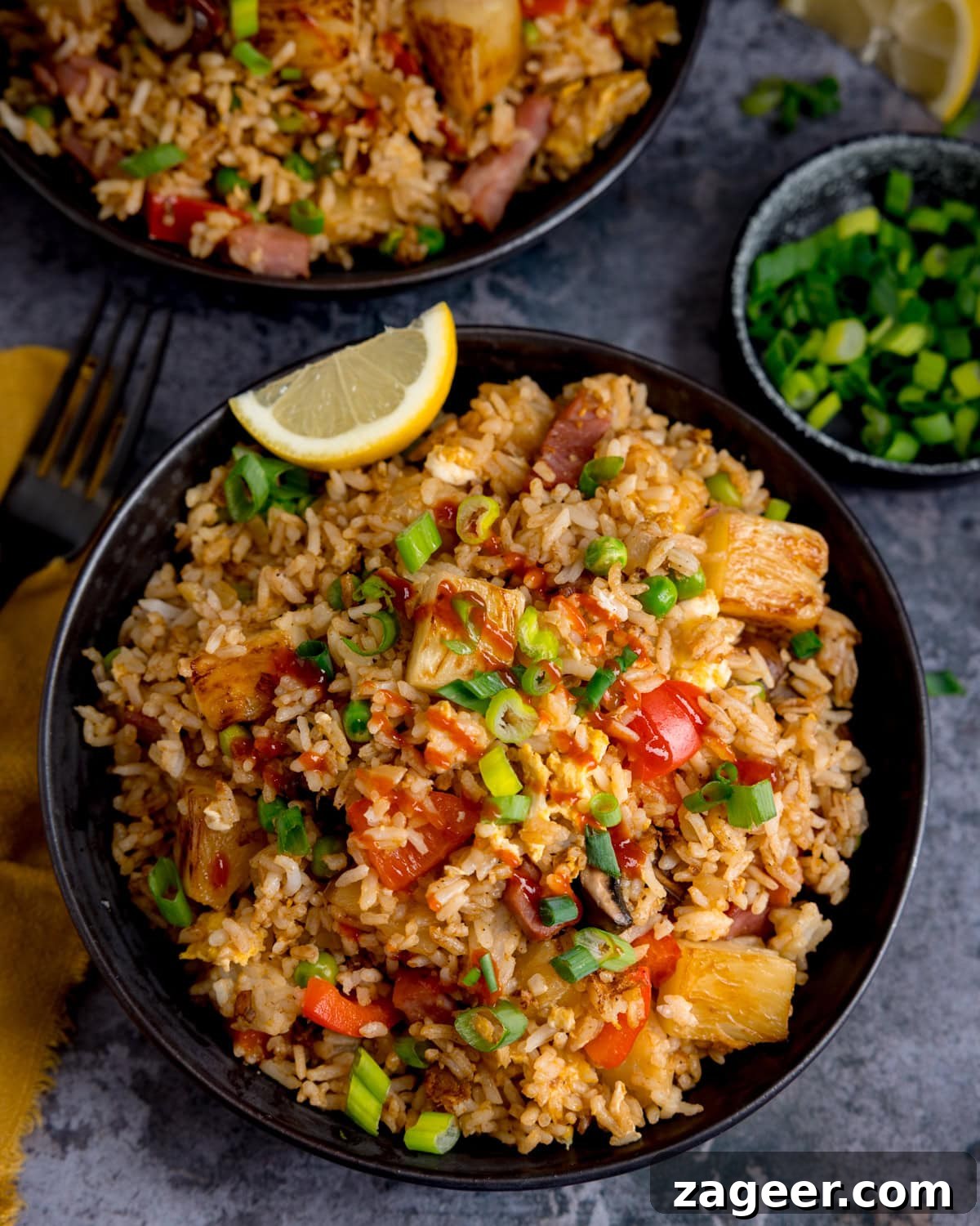 Overhead bowl of Ham and Pineapple Fried Rice garnished with spring onions and a lemon wedge