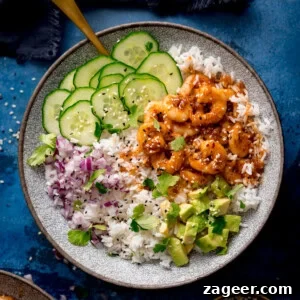Honey Garlic Prawn Rice Bowl Recipe for Quick Weeknight Meals 11 A bowl of white rice topped with cooked honey garlic prawns, sliced cucumber, chopped red onion, diced avocado, fresh coriander, and sesame seeds.