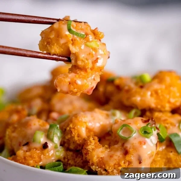 Honey Garlic Prawn Rice Bowl Recipe for Quick Weeknight Meals 17 Crispy shrimp being lifted out of a bowl with chopsticks. Shrimp is covered with bang bang sauce.