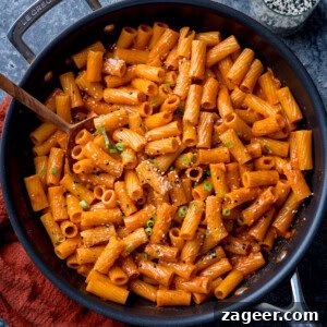 Spicy Gochujang Cream Pasta Recipe You’ll Love 12 Overhead square image of a frying pan filled with creamy Gochujang pasta topped with grated Parmesan, black pepper, and chopped spring onions.