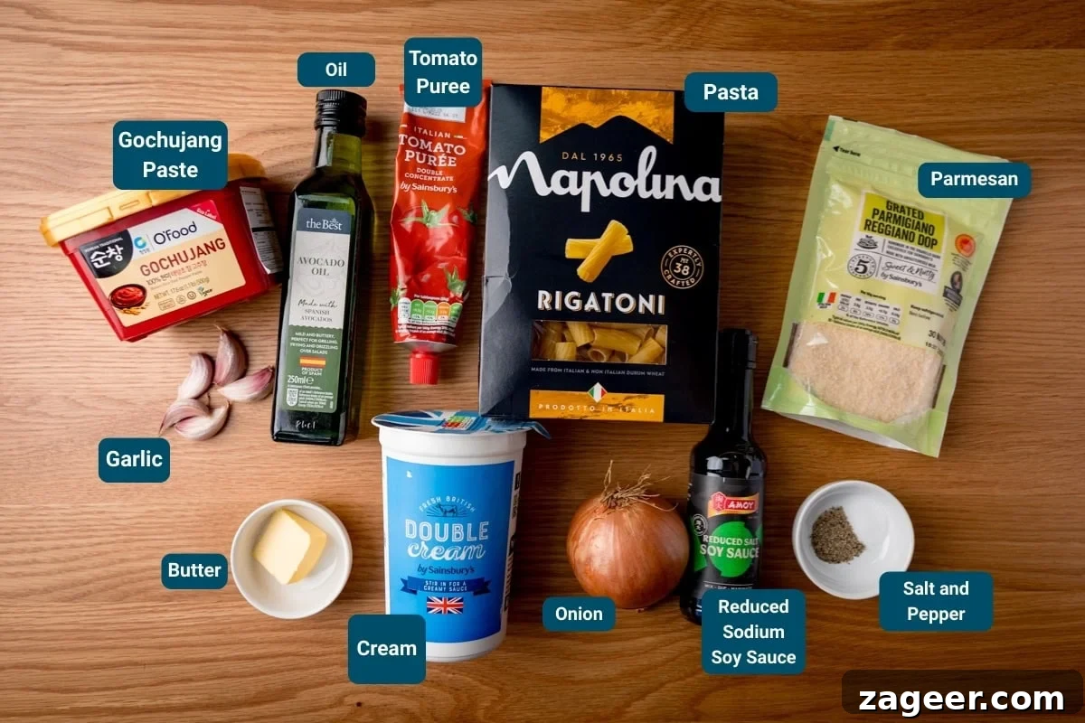 Spicy Gochujang Cream Pasta Recipe You’ll Love 4 Ingredients for Gochujang Pasta on a wooden surface. All ingredients labelled, including rigatoni, cream, tomato purée, parmesan, gochujang paste, soy sauce, garlic, butter, onion, oil, salt and pepper.