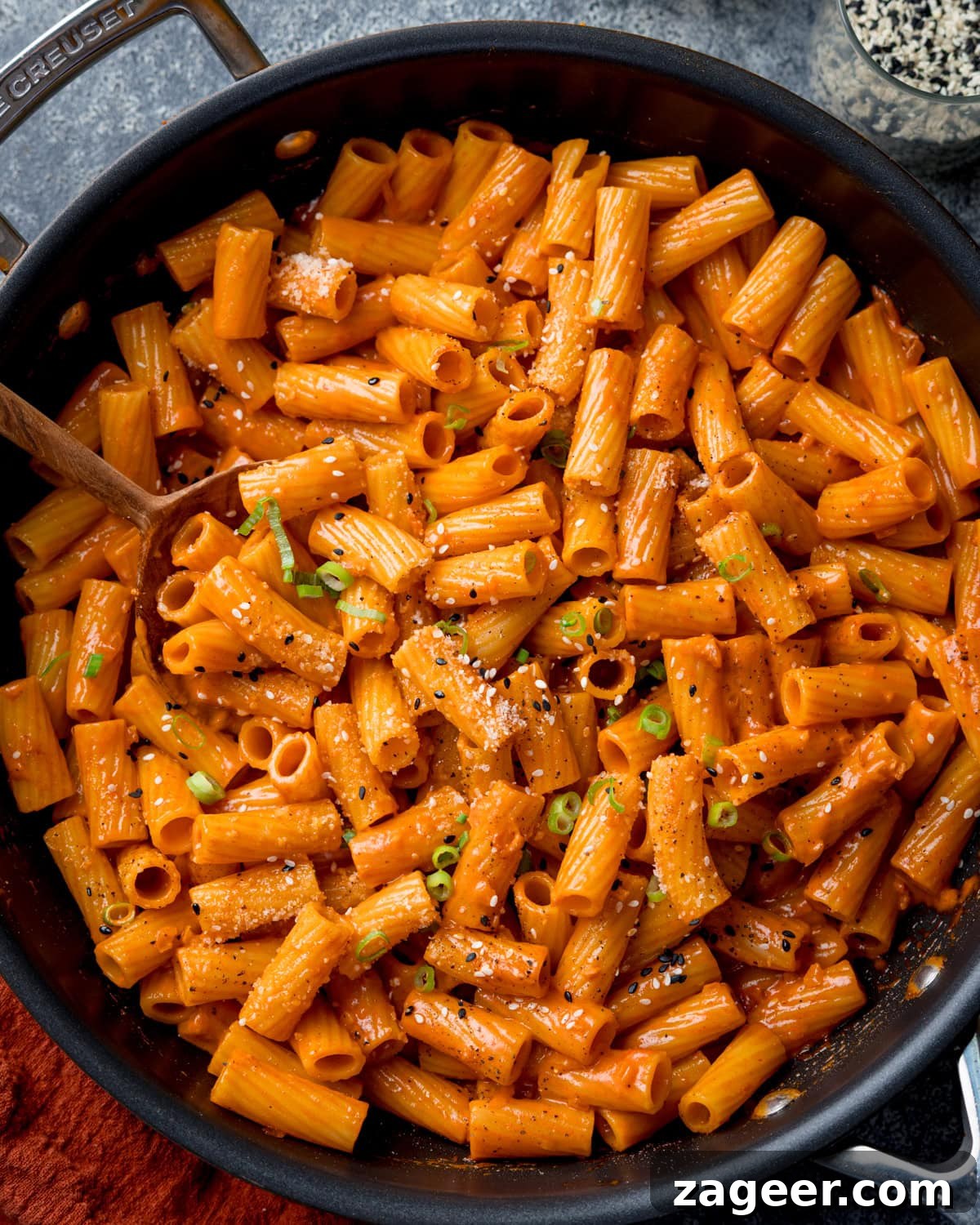 Spicy Gochujang Cream Pasta Recipe You’ll Love 5 Overhead image of a frying pan filled with creamy Gochujang pasta topped with grated Parmesan, black pepper, and chopped spring onions. There is a wooden spoon resting in the pan.