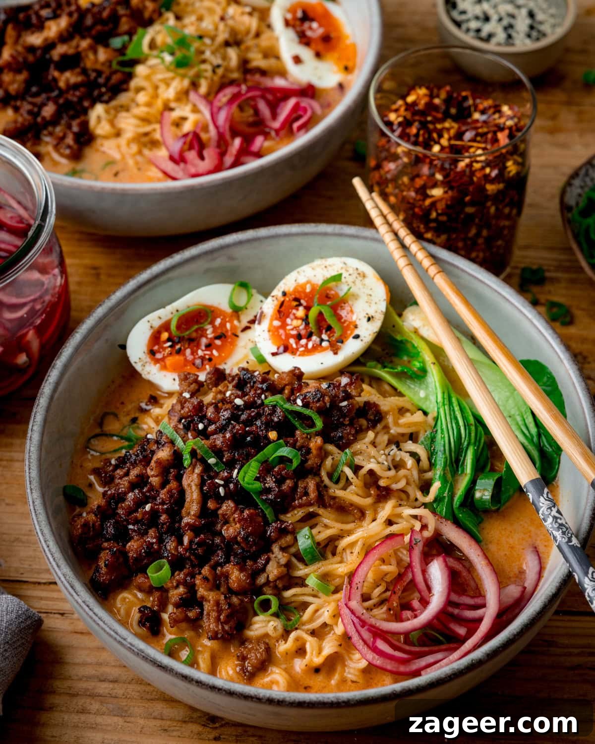 Spicy Pork Curry Ramen Recipe for Bold Flavor 2 Two bowls of Curry Ramen with Spicy Pork, noodles, soft-boiled eggs, pak choi, pickled onions, and spring onions are served with chopsticks on a wooden table.