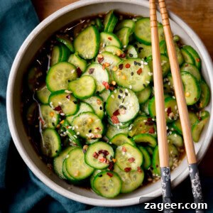 Crisp Asian Cucumber Salad with Sesame Ginger Dressing 6 Overhead square image of a bowl of Asian Cucumber Salad with sliced cucumbers in a seasoned soy-sesame dressing, with sesame seeds and chilli flakes, with chopsticks resting on the bowl.