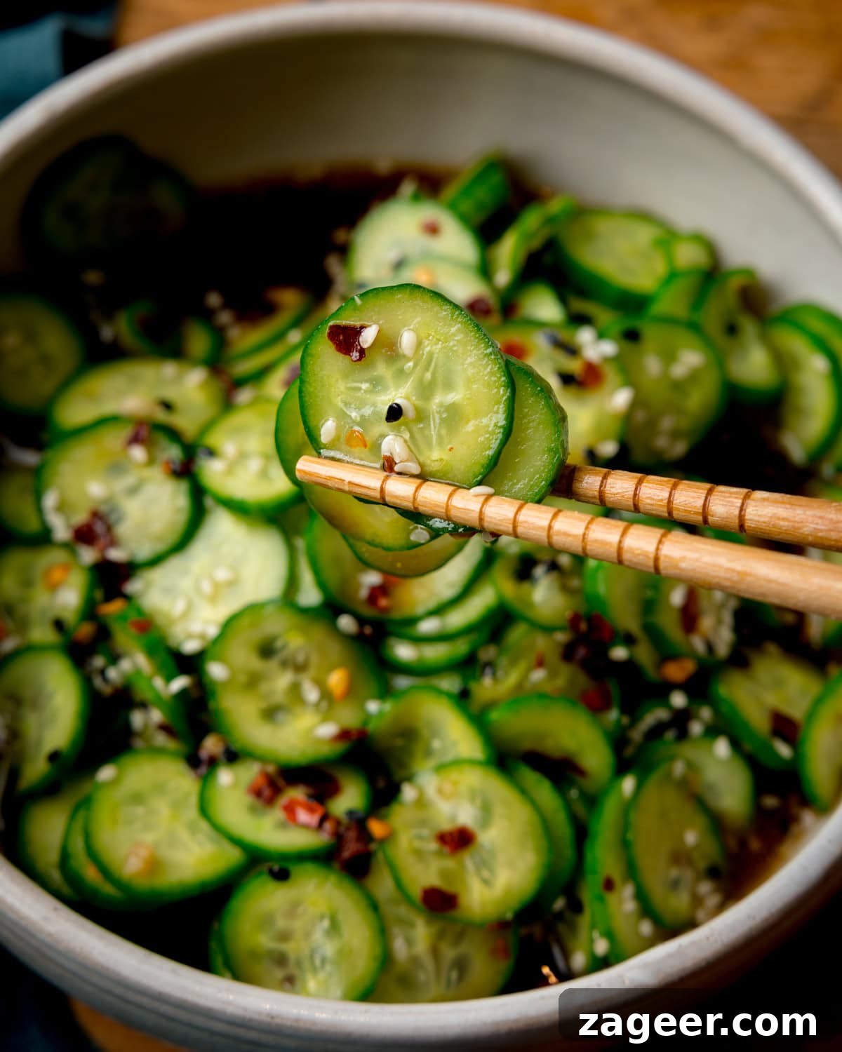 Crisp Asian Cucumber Salad with Sesame Ginger Dressing 5 Chopsticks hold a slice of cucumber above a bowl of Asian Cucumber Salad.
