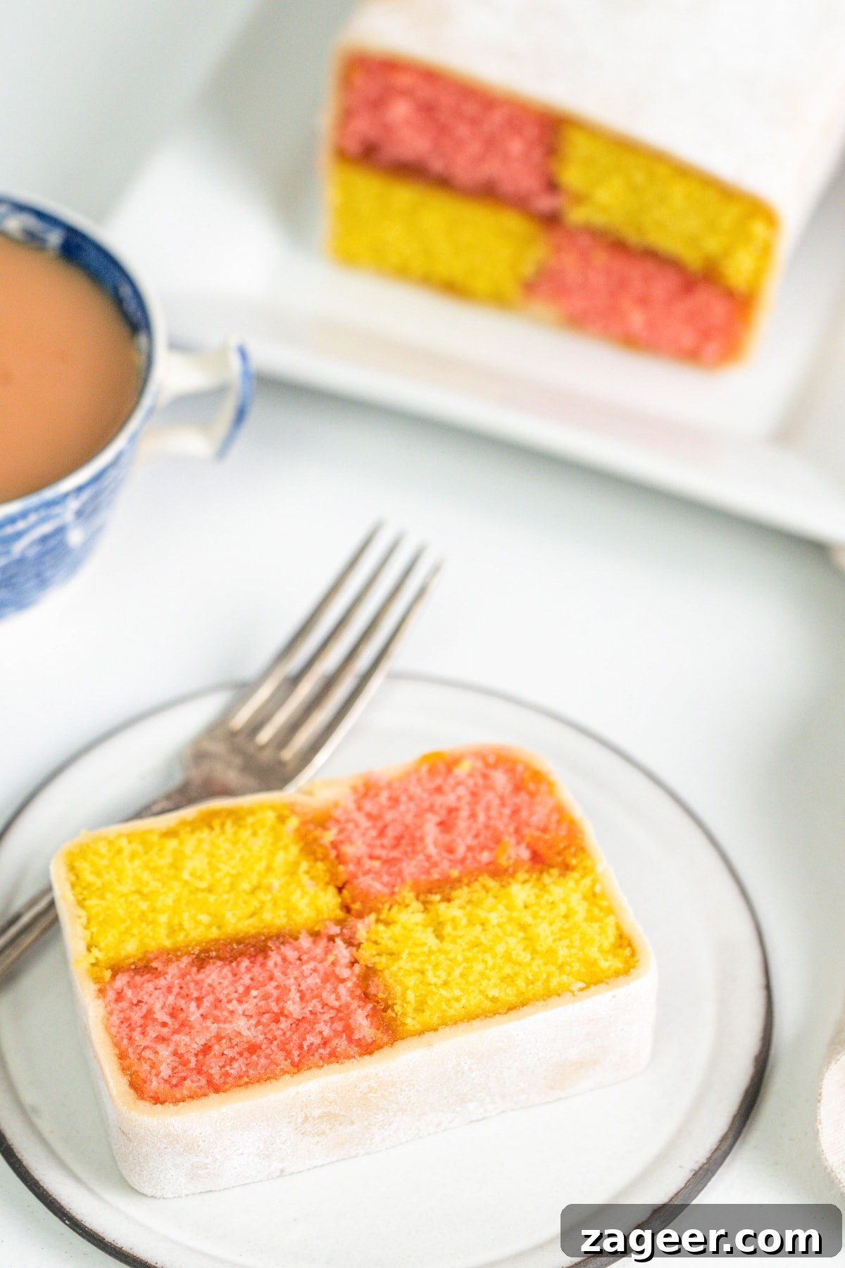 Perfect Battenberg Cake Recipe: Step-by-Step Guide 2 Slice of battenberg cake on a plate with a cup of tea and more battenberg in the background.
