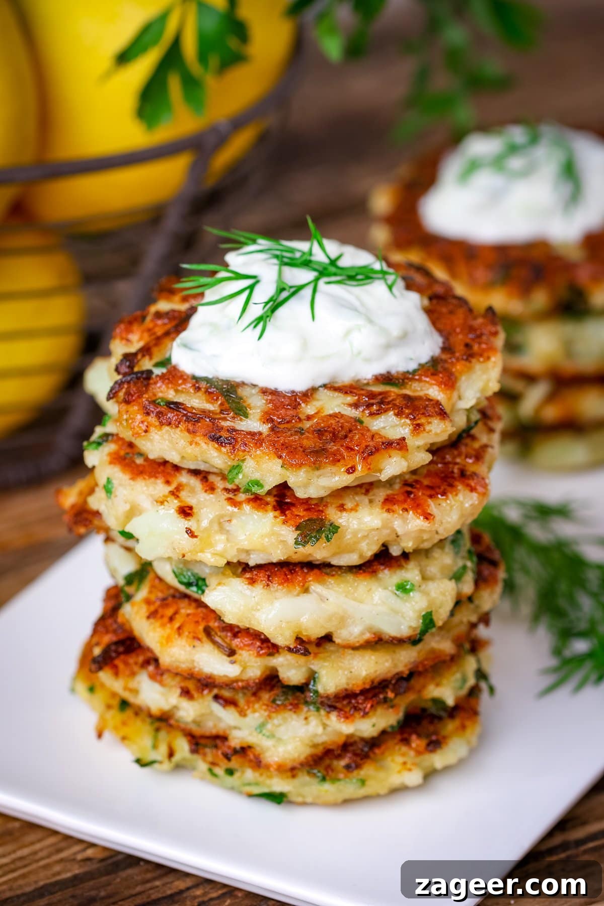 Stack of cauliflower fritters on a white plate, topped with tzatziki