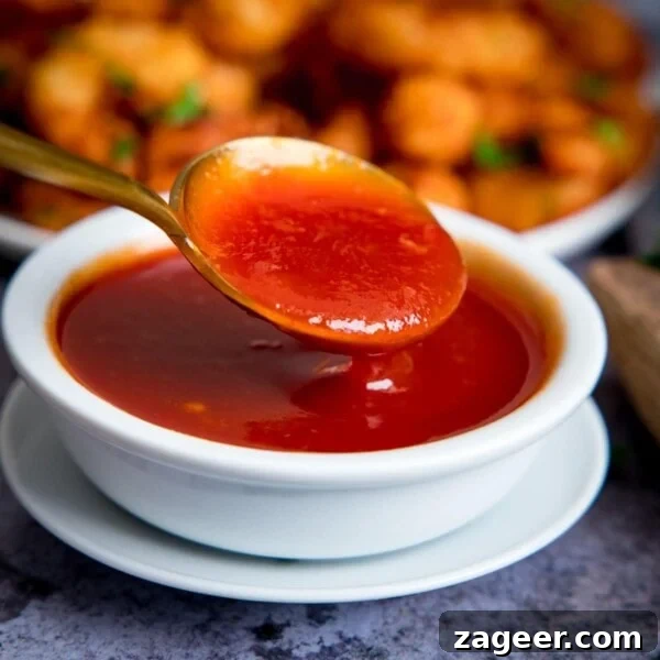 Spoonful of sweet and sour sauce being taken from a small white bowl of sauce.