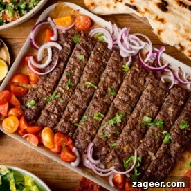 11 Fresh Spring Dinners Ready in 30 Minutes or Less 14 A tray of Sheet Pan Kebabs garnished with chopped parsley, red onion, and cherry tomato halves, served with flatbreads and salad on a wooden table.