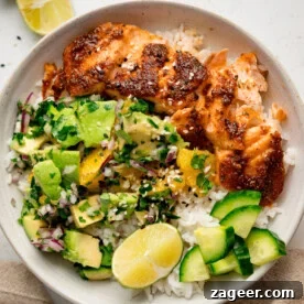 11 Fresh Spring Dinners Ready in 30 Minutes or Less 6 A white bowl on a white surface with spiced salmon, rice, avocado orange salad, cucumber, lime wedges, and a sprinkle of sesame seeds.