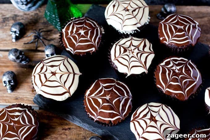 Spider Web Chocolate Cupcakes for Halloween Parties 3 Chocolate Halloween cupcakes with spiderweb patterns in the topping placed on a dark slate background with toy skulls and spiders on a wooden board.