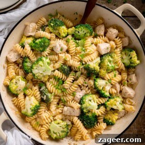 One-Pot Chicken and Broccoli Pasta Dinner in 30 Minutes 7 Overhead shot of chicken and broccoli pasta in a white cast iron pan with a wooden spoon sticking out. The pan is on a wooden table with a white napkin