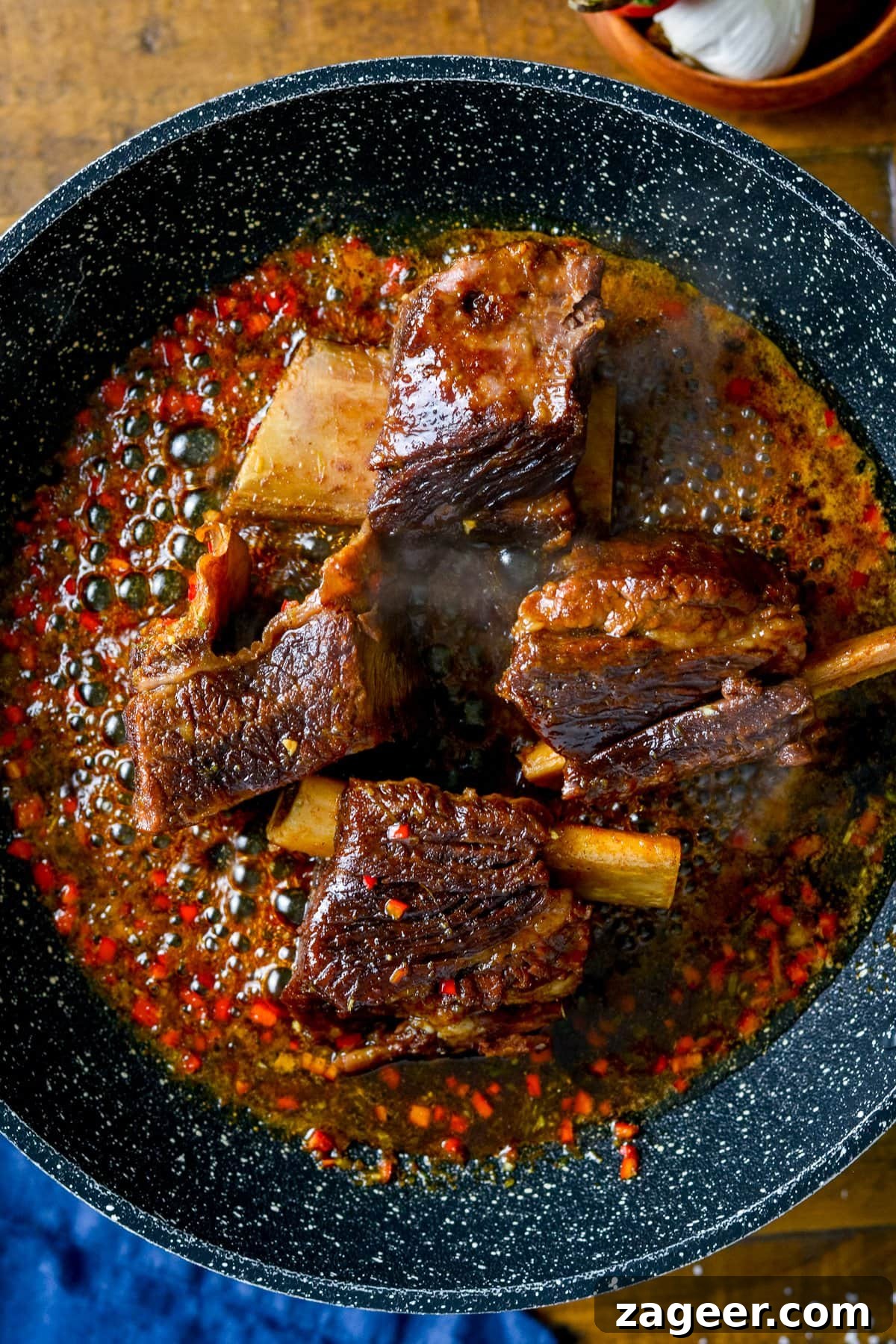 Overhead photo of sticky short ribs in a frying pan with sauce bubbling around the short ribs.