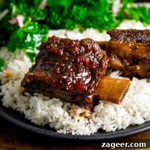 Sticky chilli-glazed short ribs on a bed of rice on a dark plate with kale in the background.