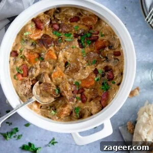 Creamy Slow-Cooked Pork Casserole Recipe for Comforting Dinners 7 Overhead image of creamy pork and bacon casserole in a white casserole pan, on a light blue surface. There is a spoonful of the casserole being taken. There is some torn bread and parsley on the table, around the casserole pan.