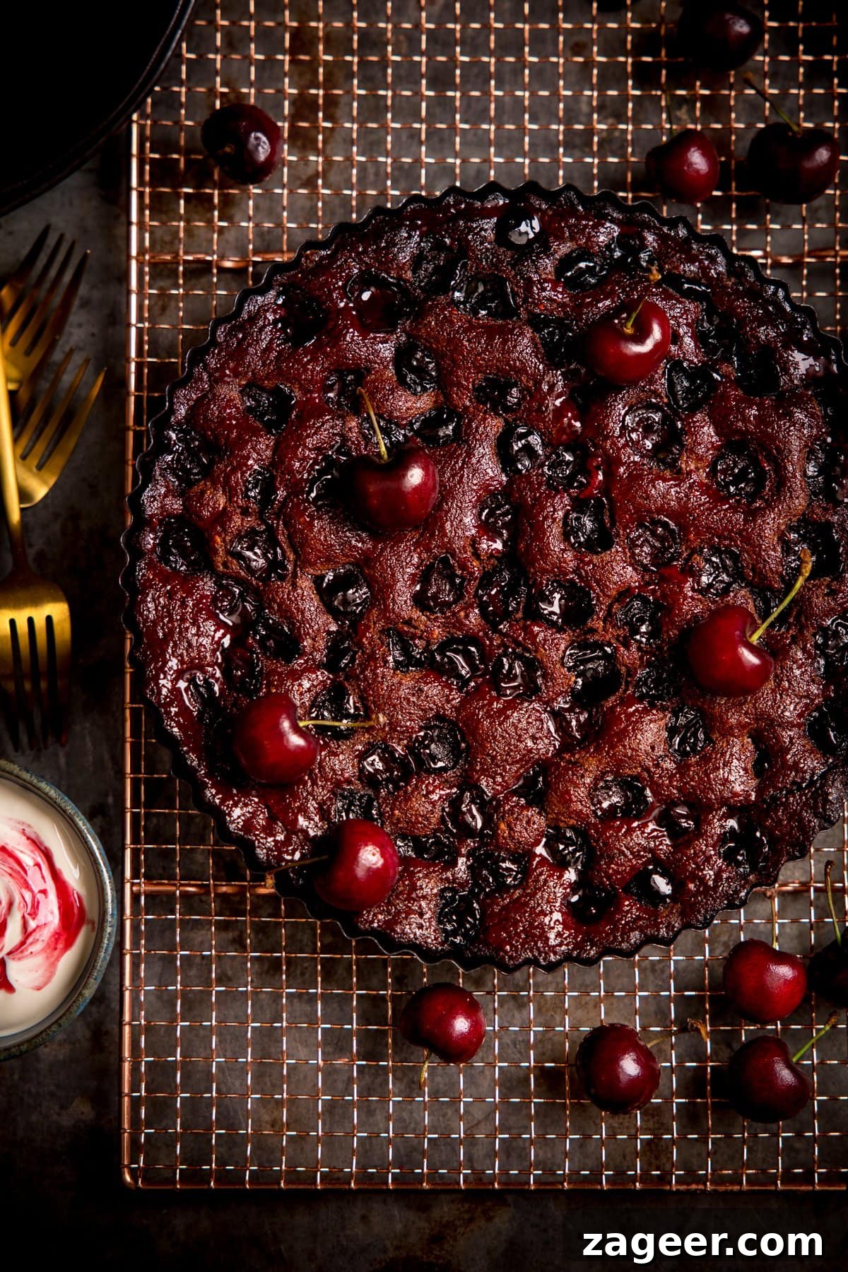 Decadent Chocolate Cherry Layer Cake Recipe 2 Overhead image of Chocolate Cherry Cake on a wire rack with cherries scattered around.