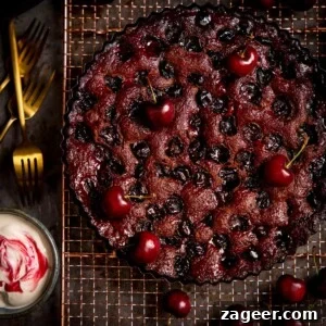 Decadent Chocolate Cherry Layer Cake Recipe 8 Chocolate Cherry Cake on a wire rack with cherries scattered around.