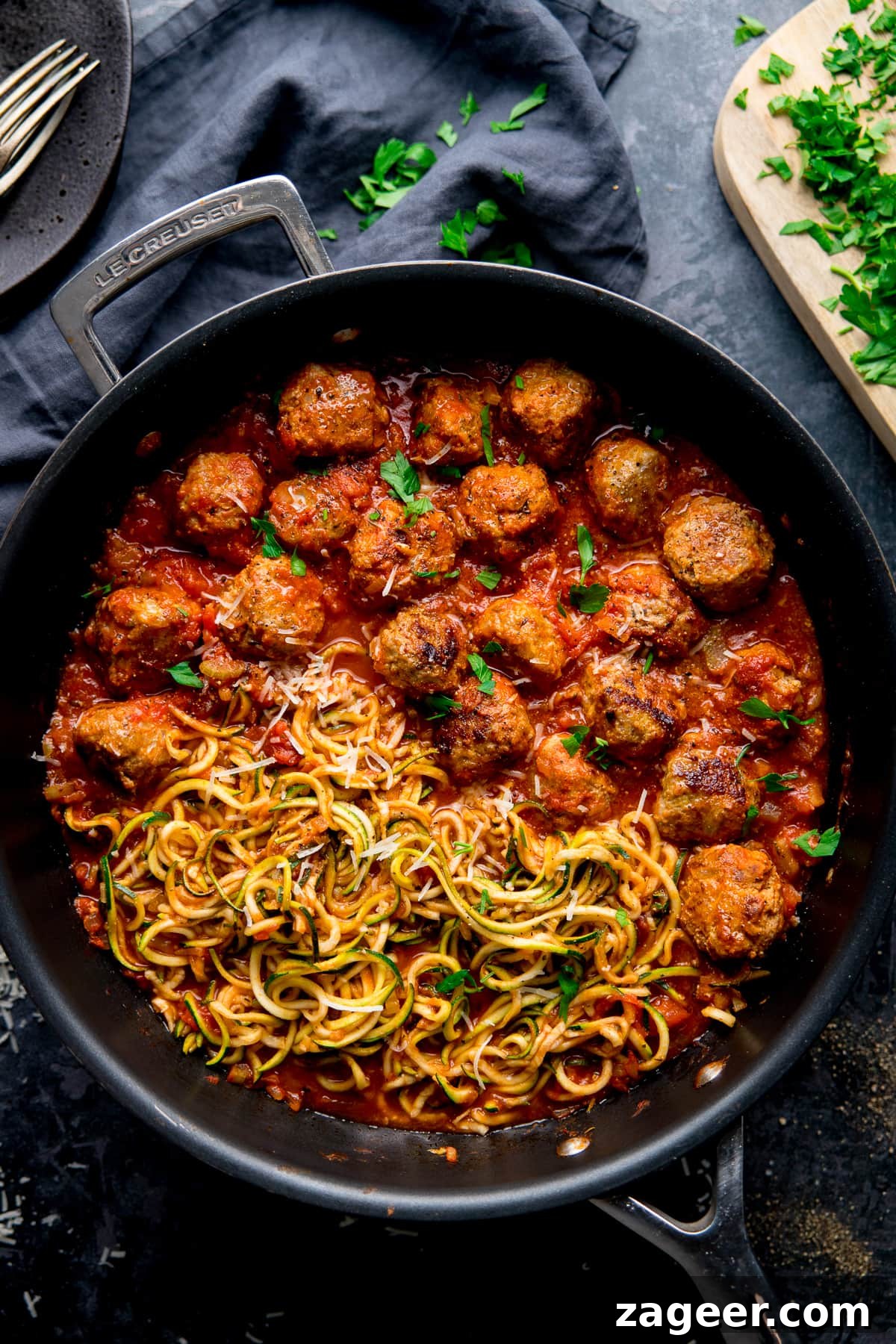 One-Pot Turkey Meatballs with Zucchini Noodles (Courgetti) 6 Turkey meatballs and courgetti in a pan topped with parsley, on a dark background.