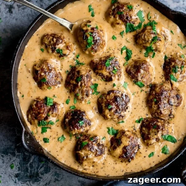 One-Pot Turkey Meatballs with Zucchini Noodles (Courgetti) 7 Swedish meatballs and gravy in a pan on a mottled blue background.