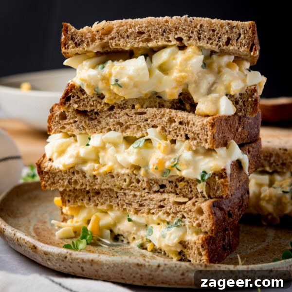 Spicy Scrambled Eggs with Smashed Beans Breakfast Bowl 10 Three egg mayonnaise sandwich halves on brown bread, stacked on a plate.