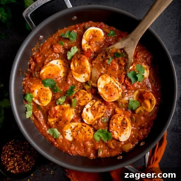 Spicy Scrambled Eggs with Smashed Beans Breakfast Bowl 9 A frying pan filled with spicy egg curry, topped with halved boiled eggs and garnished with fresh coriander.