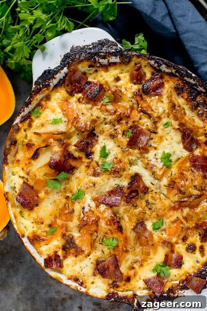 Overhead photo of Squash and Potato Gratin in a grey and white baking dish with a scoop taken out, topped with bacon