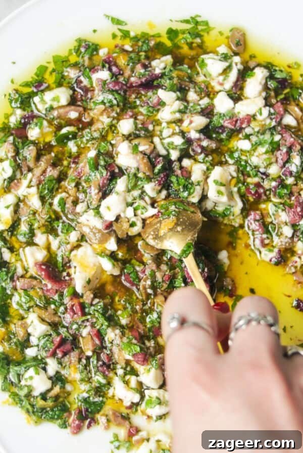 Hand mixing ingredients for Greek dipping oil in a large white plate.